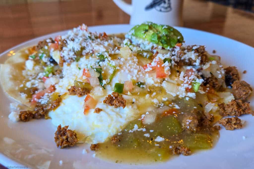 Huevos rancheros with chorizo, green chile sauce, queso fresco and avocado slices on a white plate