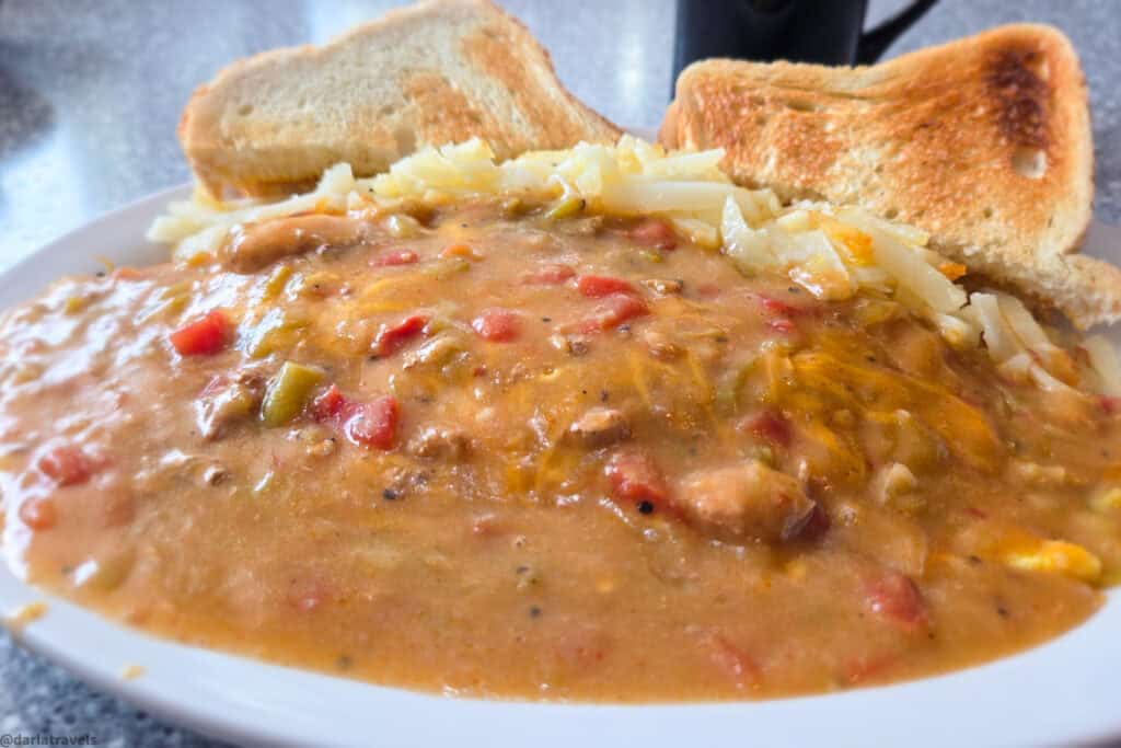Hash browns and toast smothered in chunky green chile and cheese sauce on a white oval plate