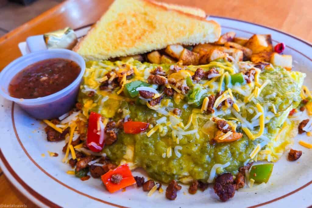 Green chili chorizo omelette topped with peppers and cheese, served with breakfast potatoes, toast and salsa at a Moab grill