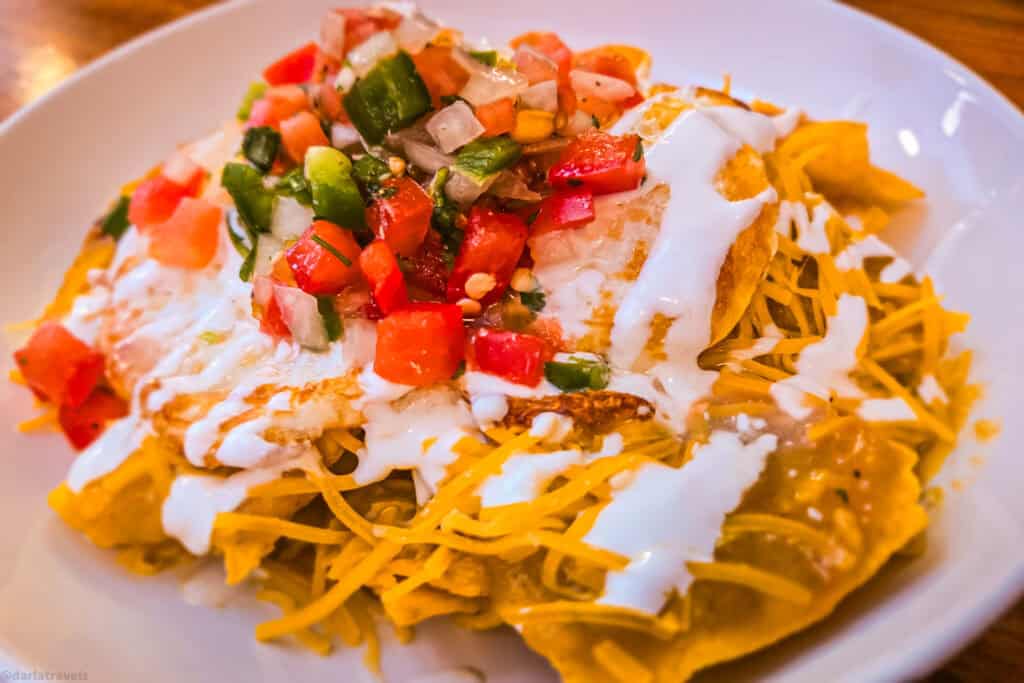 Chilaquiles close-up with fried eggs, shredded cheese, crema and fresh pico de gallo on a white plate.