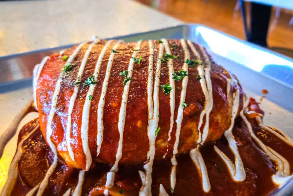 Smothered breakfast burrito covered in red ranchero sauce with crema drizzle and herbs on a metal tray at a Moab café