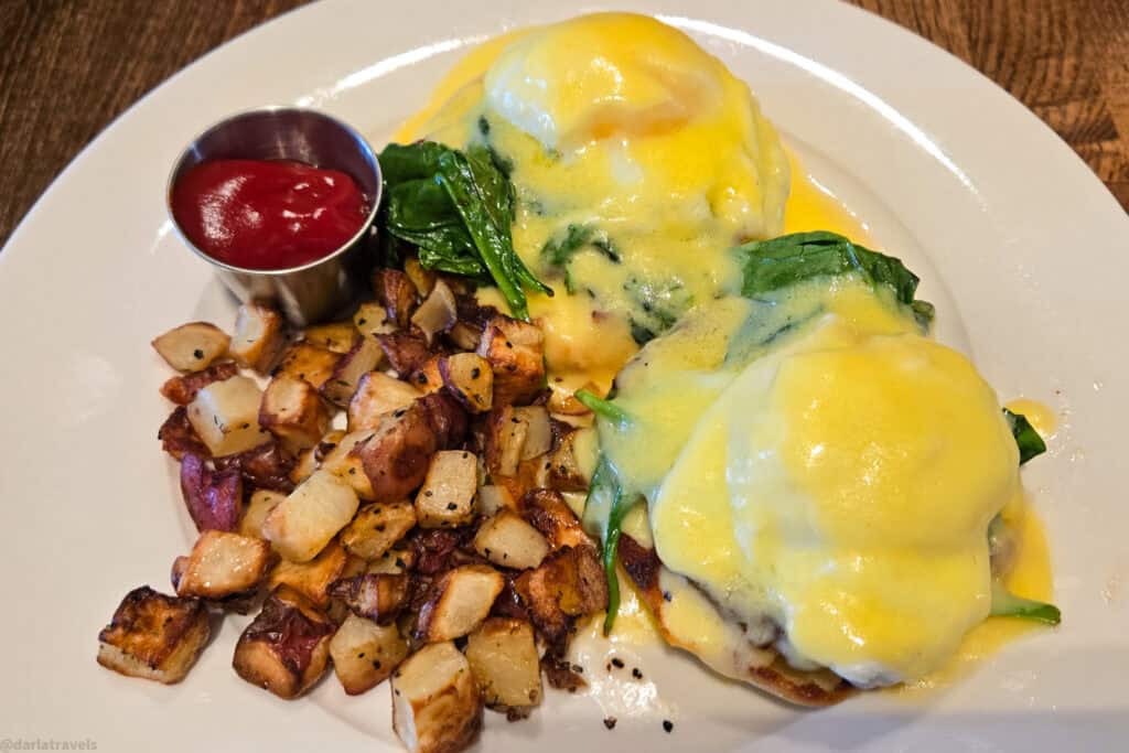 Eggs Benedict with sautéed spinach, crispy breakfast potatoes and ketchup on a white plate at a Moab restaurant
