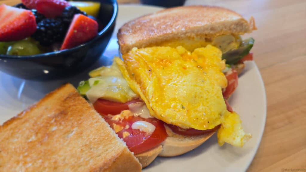 Egg and cheese sourdough breakfast sandwich with tomato and avocado, served with a fresh fruit bowl