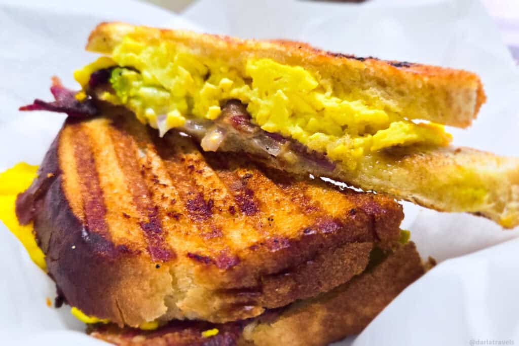 Grilled breakfast sandwich with scrambled eggs and avocado on toasted bread, cut in half to show the filling