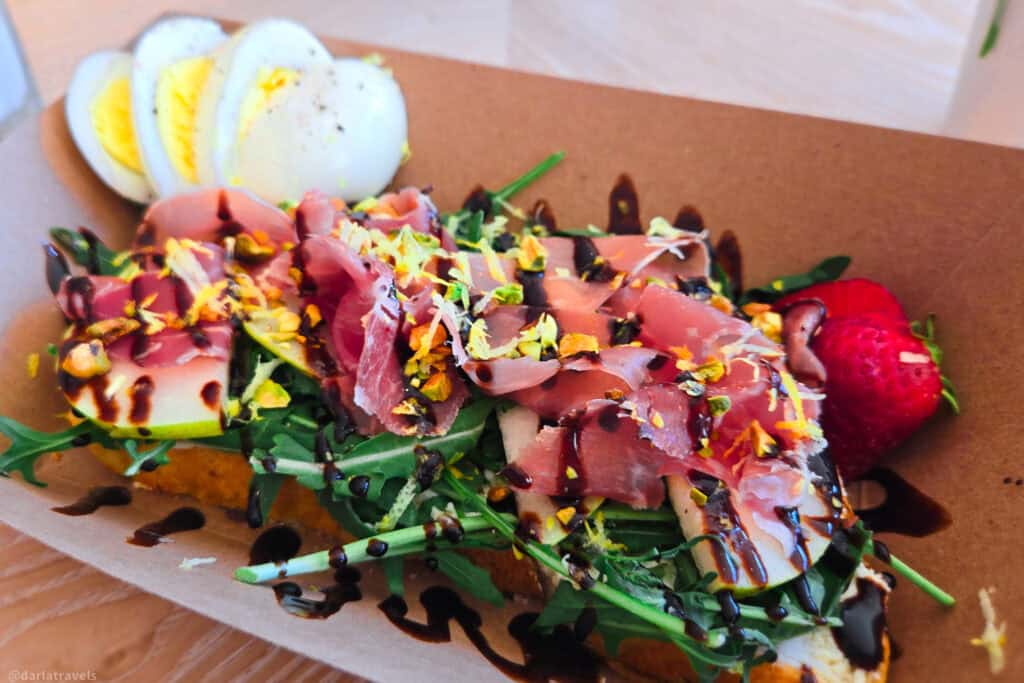 Sourdough toast topped with prosciutto, arugula, pistachios, balsamic drizzle and sliced egg with a fresh strawberry