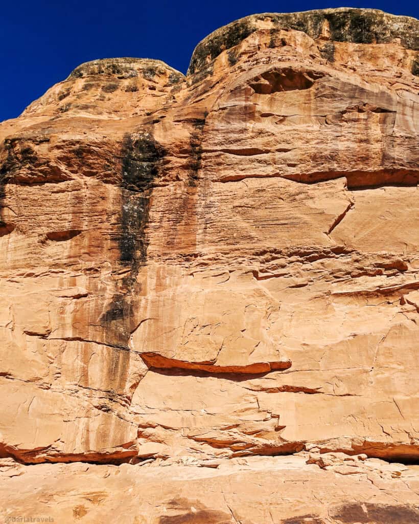Layered sandstone cliff with erosion streaks rising above the trail on a short desert hike near Moab.