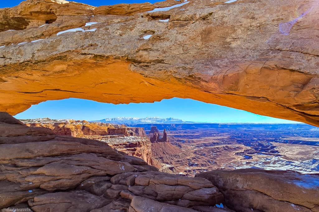 Mesa Arch framing snowy canyons and distant peaks along a short winter hike in Canyonlands National Park.