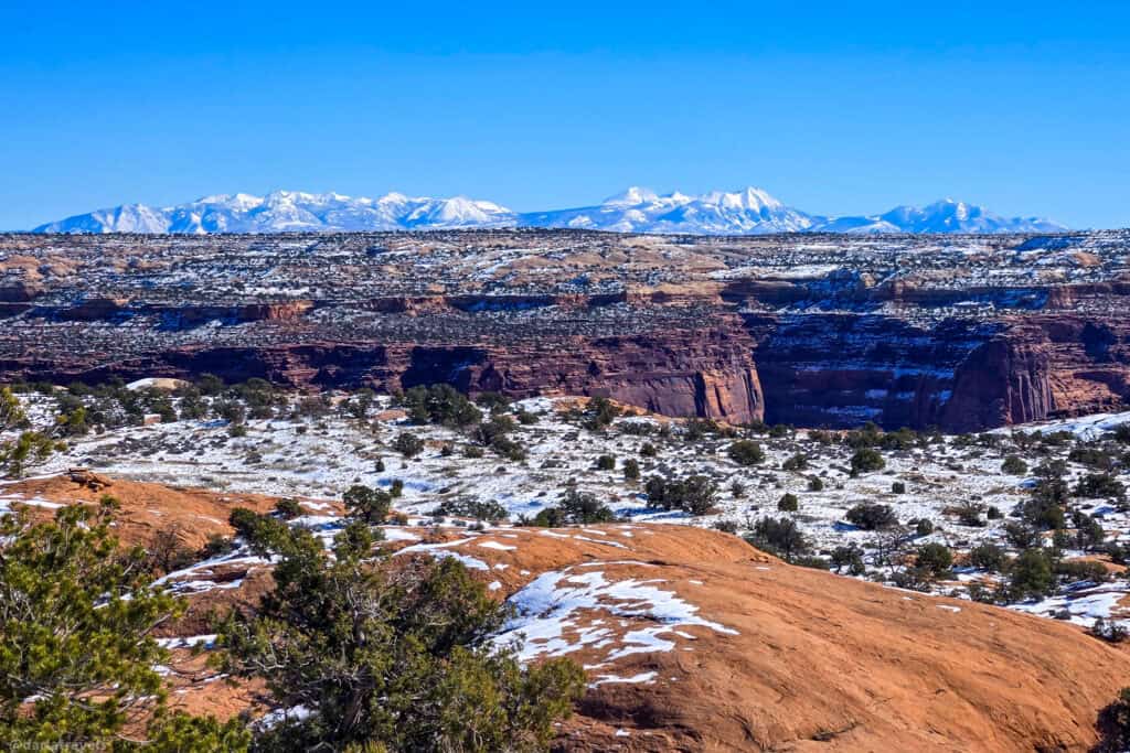 Snow-dusted red canyon opening toward distant white peaks on a short winter hike in Canyonlands National Park.