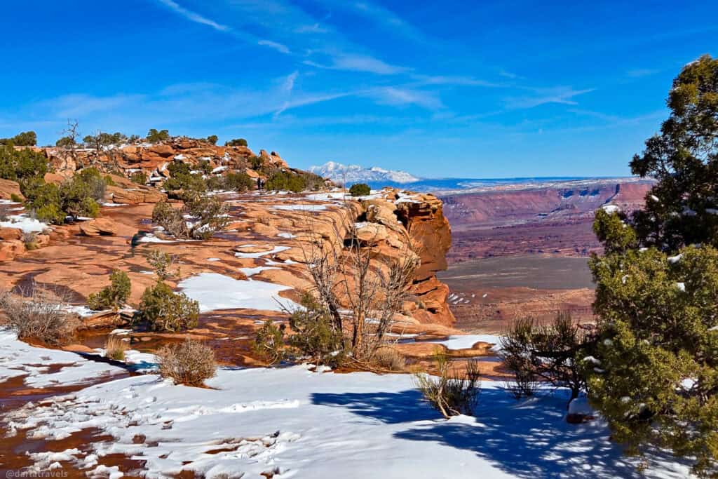 Snow‑patched sandstone cliffs and distant white peaks seen from a short winter hike in Canyonlands National Park.