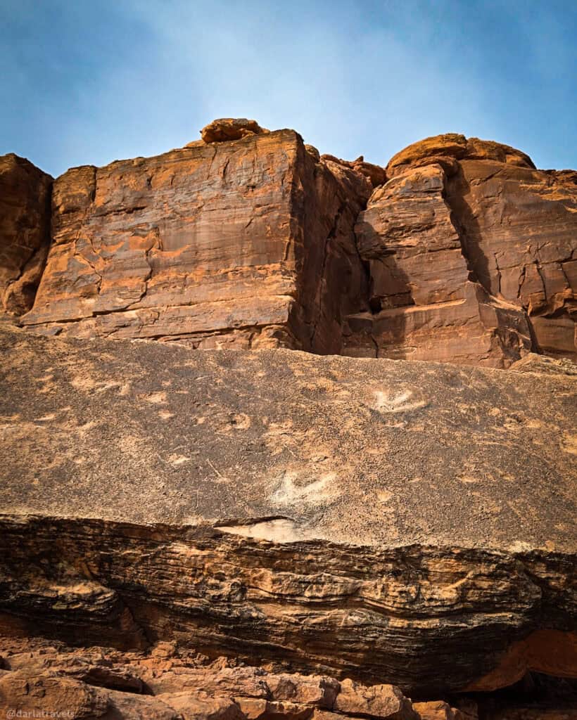 Layered sandstone wall with dinosaur footprints on a fallen panel in the foreground