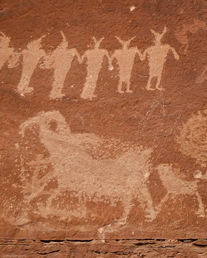 Humanoid and animal petroglyphs etched into red rock near Moab