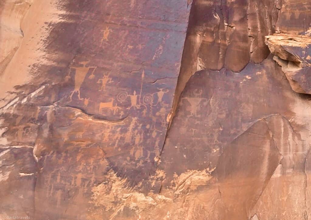 Human and animal petroglyphs etched into a tall sandstone cliff the the Highway 279 rock art site