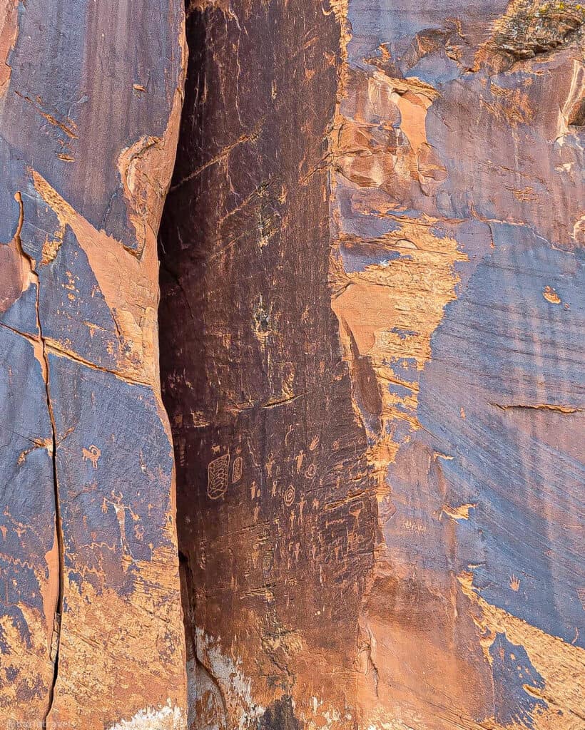 Color‑banded sandstone wall with deep cracks and mineral streaks seen along Highway 279 near Moab.