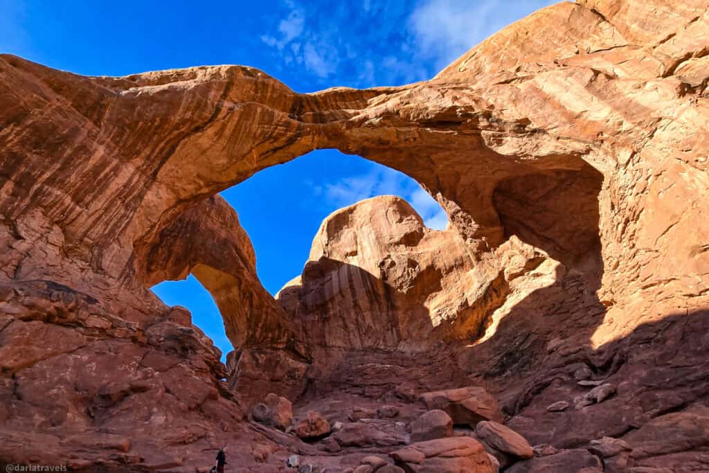 Double Arch towering over a hiker on a short trail in Arches National Park.