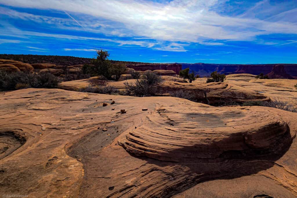 Desert rock formations with layered textures and sparse vegetation under a blue sky.