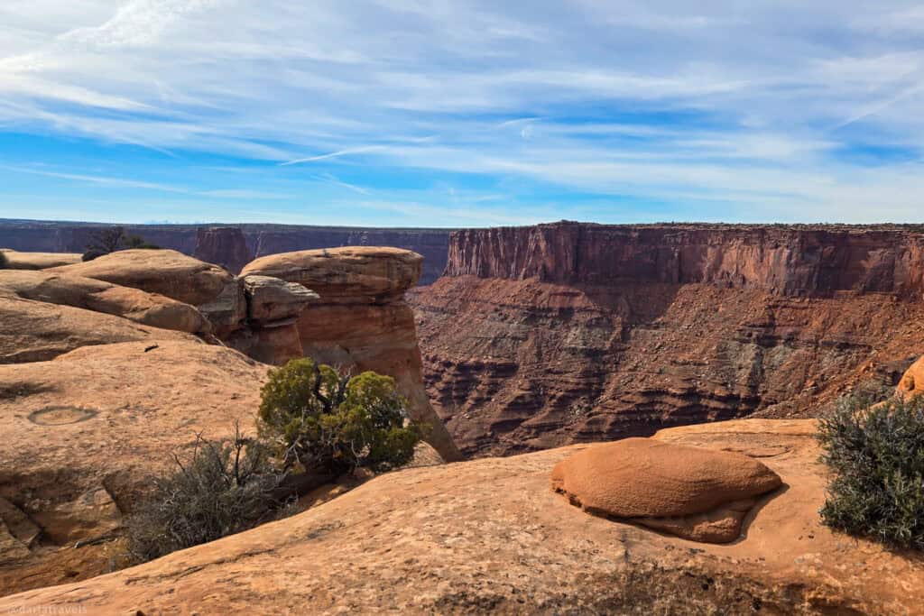 Layered red canyon walls rising beyond smooth sandstone boulders on a short hike near Canyonlands.