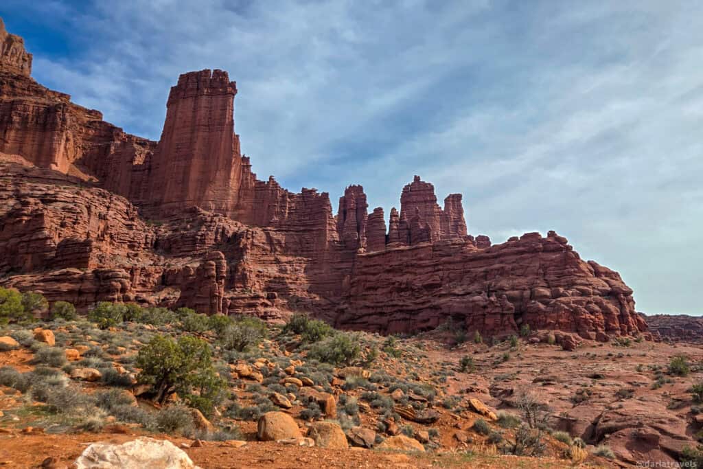 Rugged red sandstone columns rising above sparse desert vegetation on a remote Moab trail.