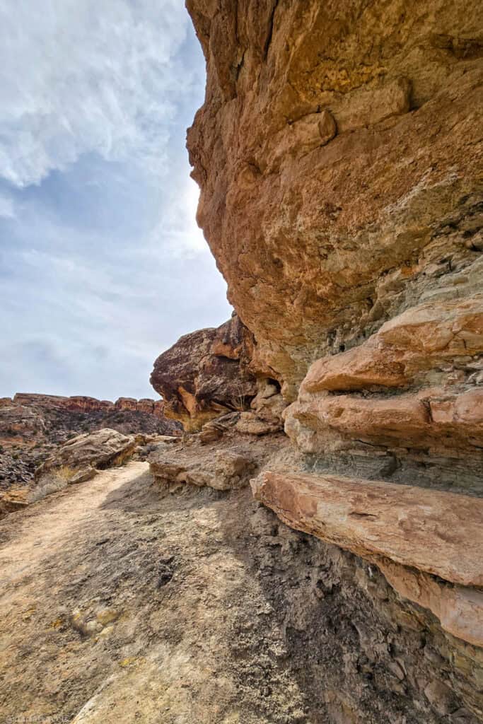 Layered sandstone cliff rising above a narrow dirt path on a quiet Moab backcountry hike.