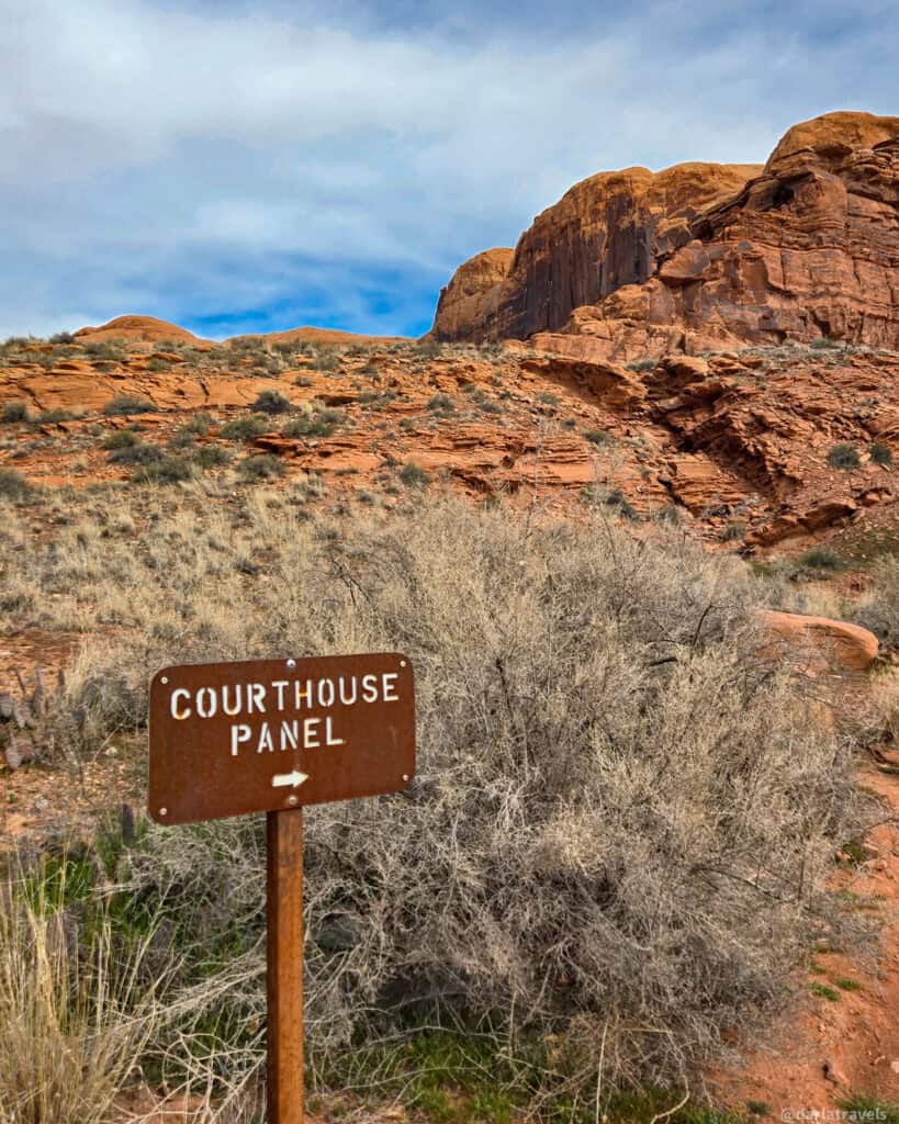 Courthouse Panel sign pointing toward sandstone cliffs along a short desert hike near Moab.