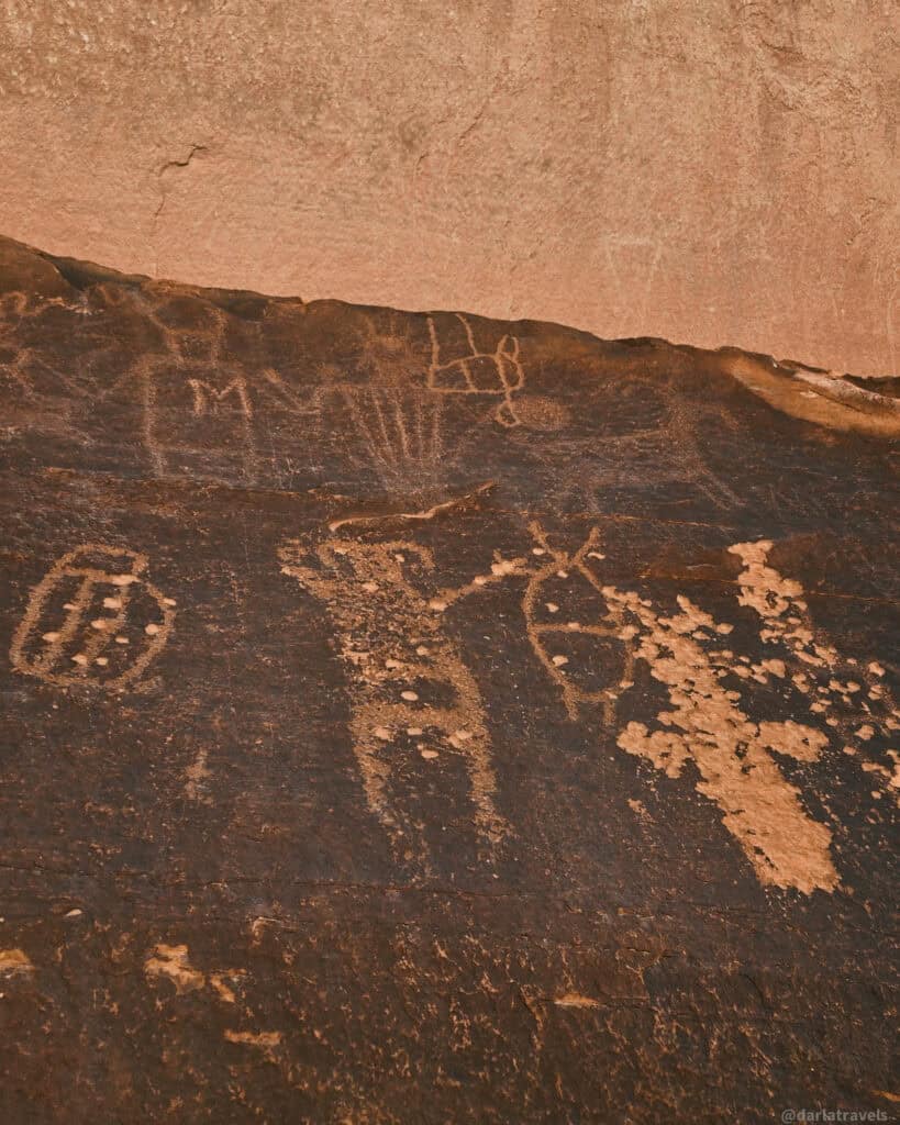 Ancient petroglyph figures carved into dark desert rock along a short walk to Courthouse Wash Panel.