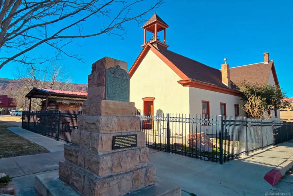 Historic LDS church, pioneer monument, and cabin set against red rock hills in Moab.