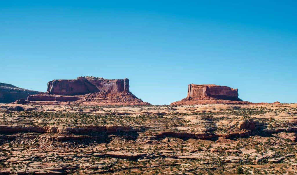 Two flat‑topped mesas rising above layered desert rock outside Moab