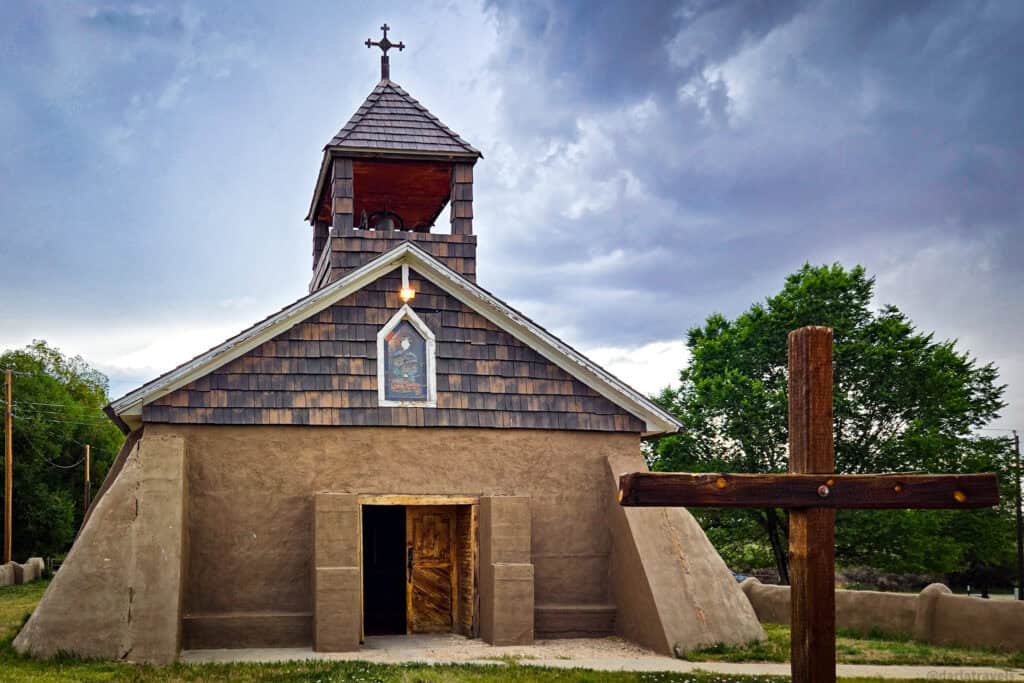 Adobe chapel with wooden bell tower and carved cross; mission church at San Acacio, Colorado