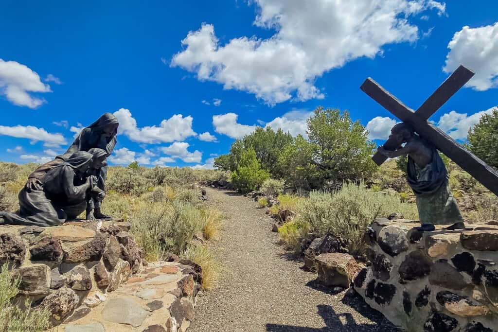 Bronze sculpture of Jesus carrying the cross past kneeling onlookers at the Stations of the Cross Shrine in San Luis Colorado