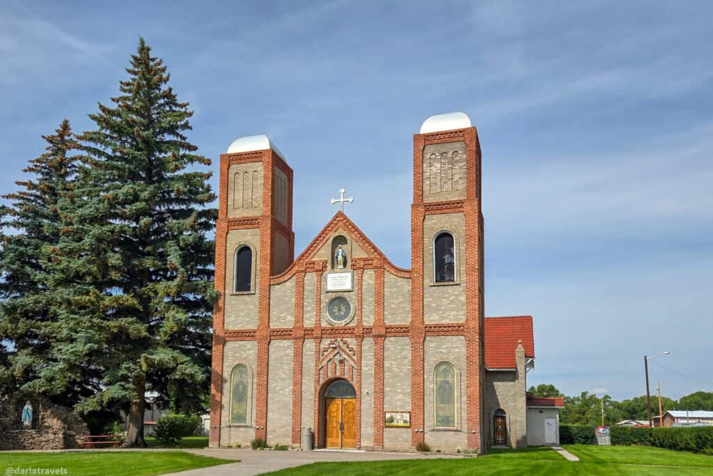 Our Lady of Guadalupe Parish Church exterior with twin brick bell towers and Virgin of Guadalupe statue in Conejos Colorado