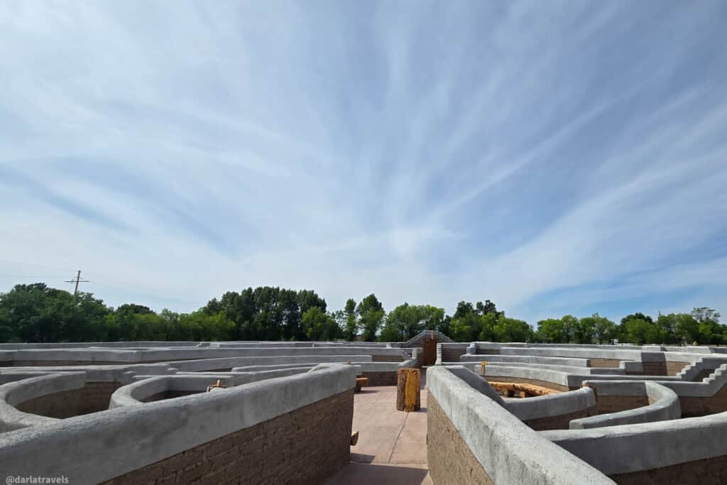 Curving adobe walls with gray plaster tops at El Santuario de los Pobladores labyrinth in Conejos Colorado under cloudy sky
