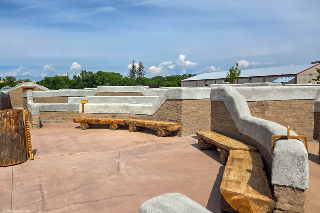 Rustic log benches and curving adobe walls inside the El Santuario de los Pobladores labyrinth in Conejos Colorado