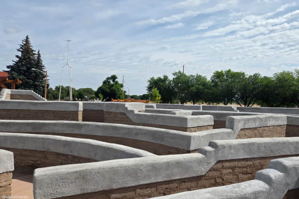 Curving adobe walls with gray plaster tops at El Santuario de los Pobladores labyrinth in Conejos Colorado under cloudy sky