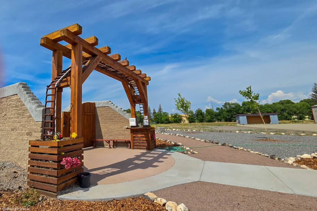 Wooden pine arch entrance with Start Here sign at El Santuario de los Pobladores adobe labyrinth in Conejos Colorado