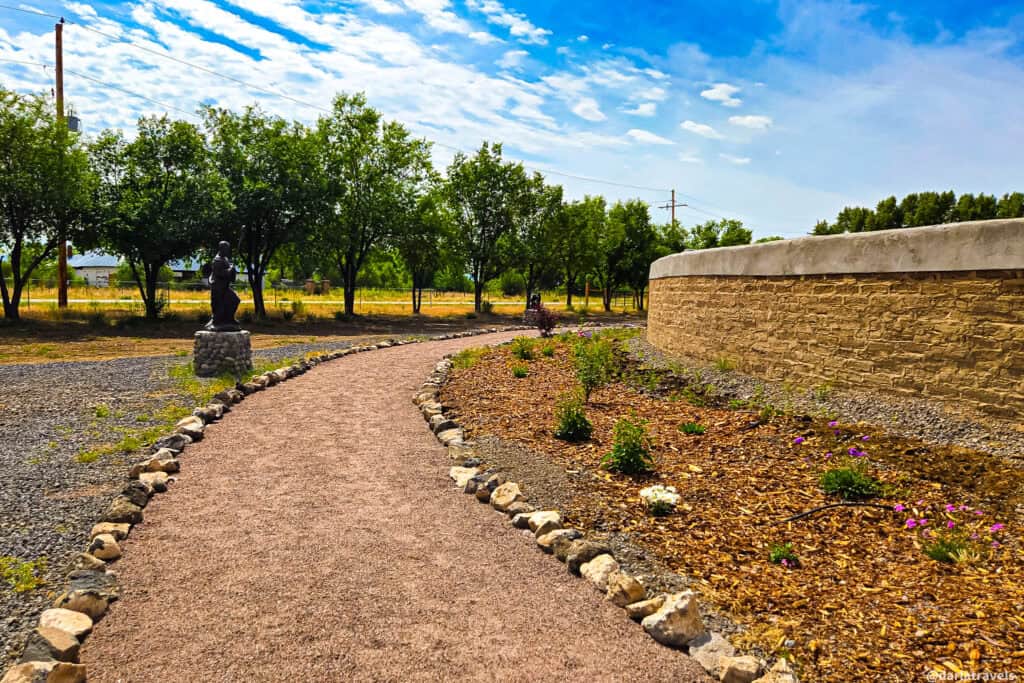 Winding path with bronze statue and adobe walls at El Santuario de los Pobladores Rosary labyrinth in Conejos Colorado