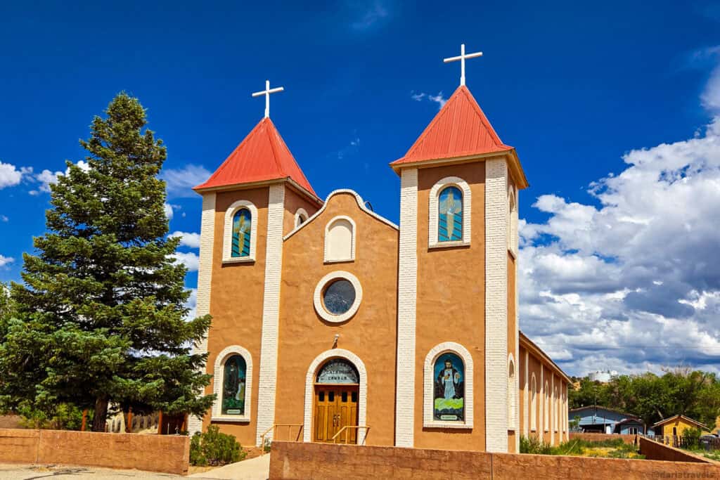 Front of tan adobe Catholic church with red towers and arched stained-glass windows in Costilla County