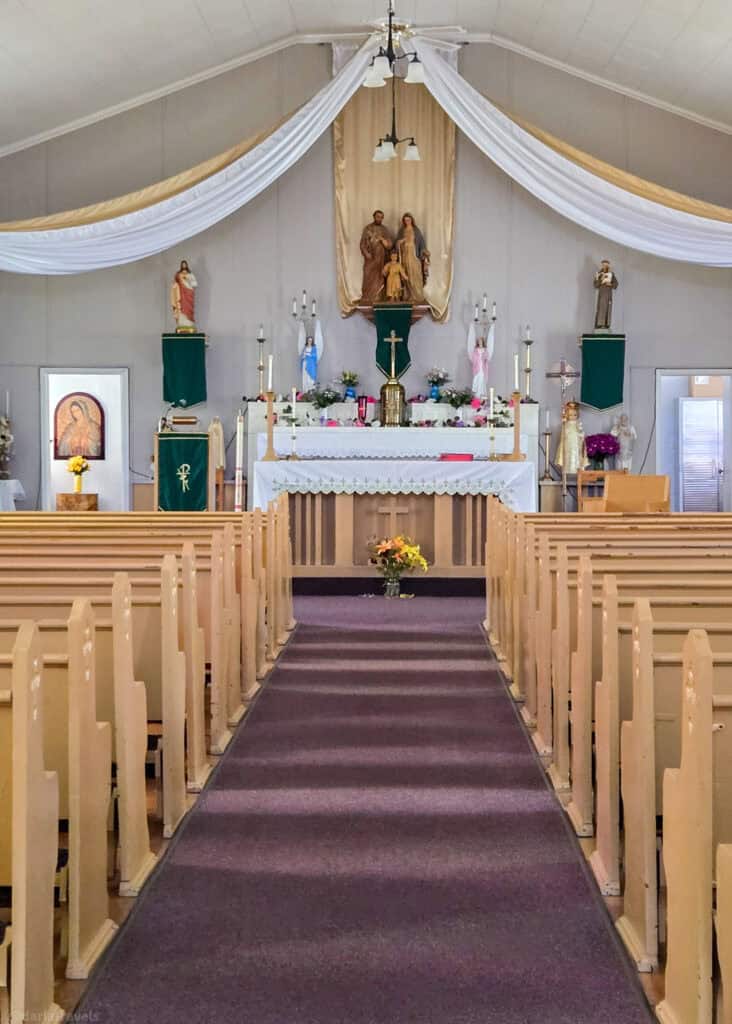 Altar view inside St. James the Less mission church with drapery, candles, and religious figures