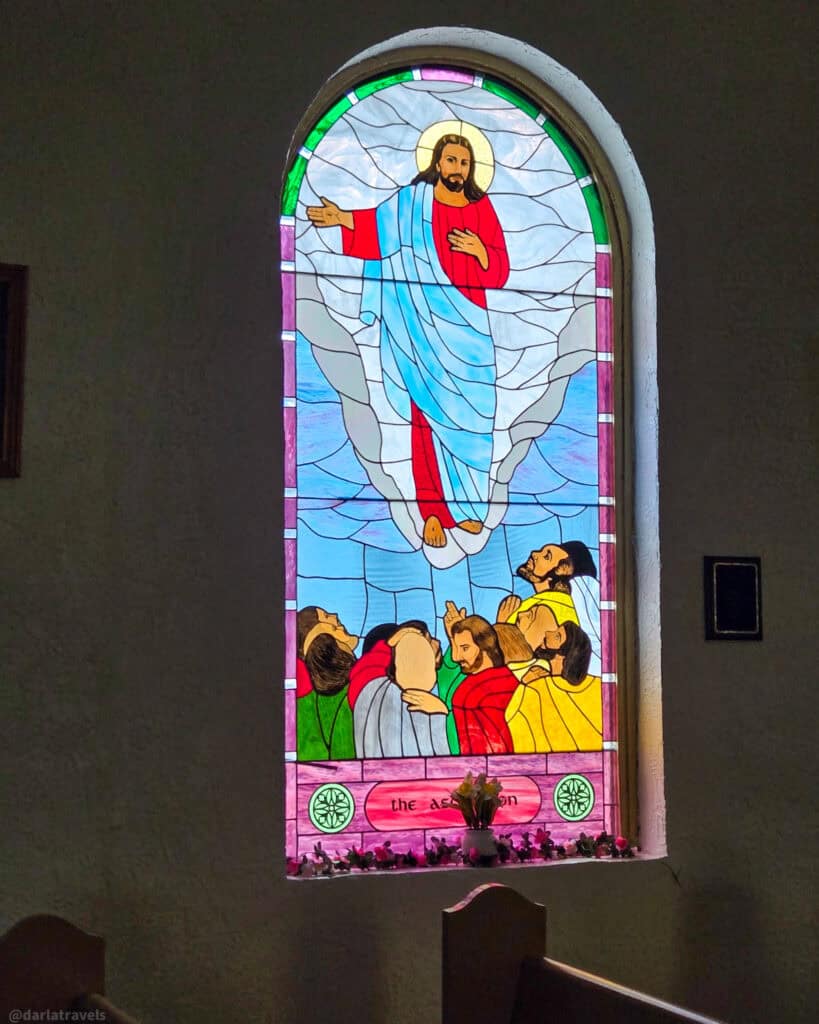 Tall arched stained-glass window showing Jesus ascending to heaven with apostles below in mission church