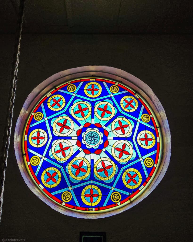 Decorative stained-glass rose window with blue background and red floral patterns in adobe mission church