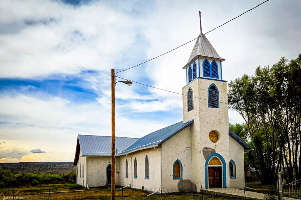 White adobe mission church with blue trim and bell tower on the plains of Costilla County, Colorado. San Pedro, Colorado