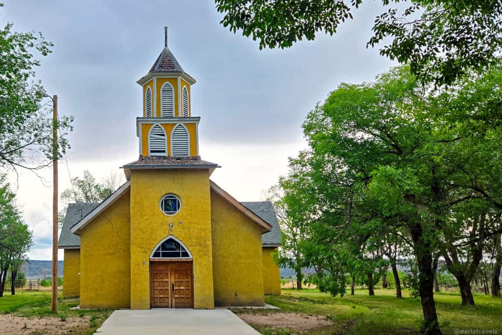 Tall yellow adobe church with louvered bell tower and Gothic door in Costilla County, Colorado