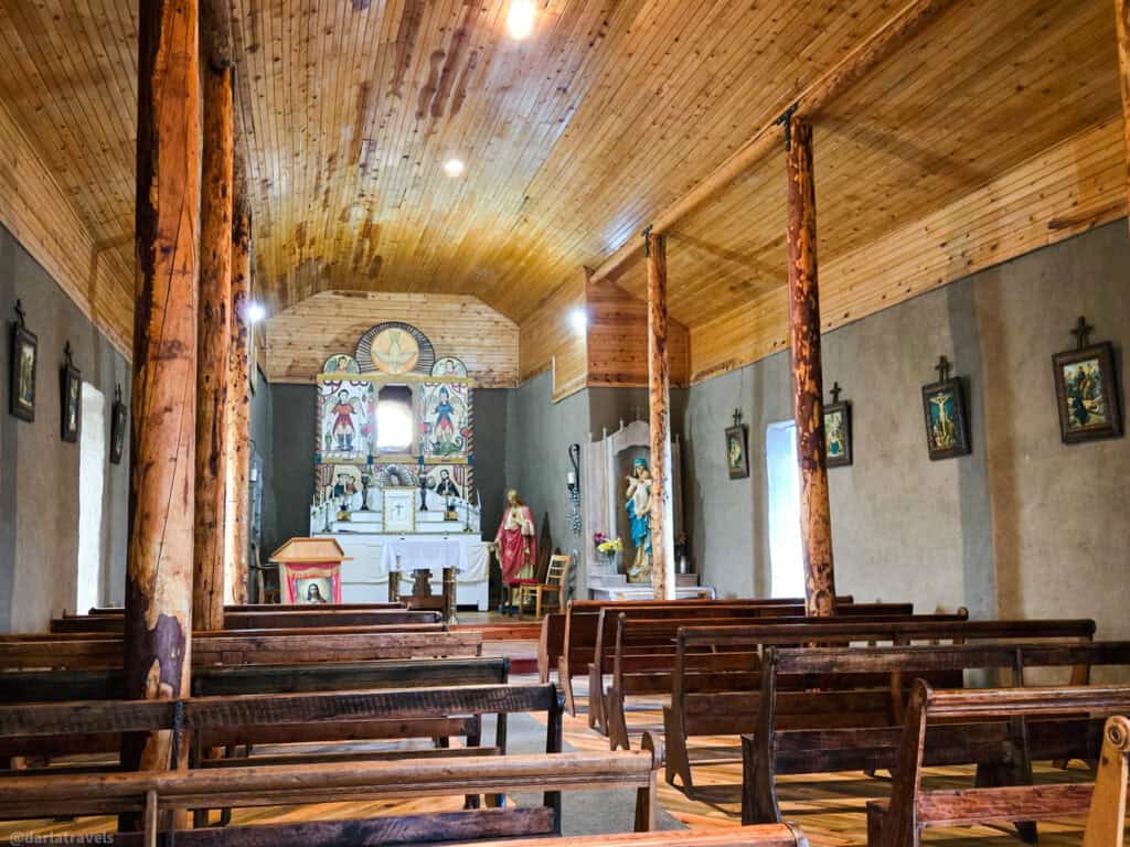 Interior of adobe mission church with rough-hewn log columns, wooden pews, and painted altar in Colorado