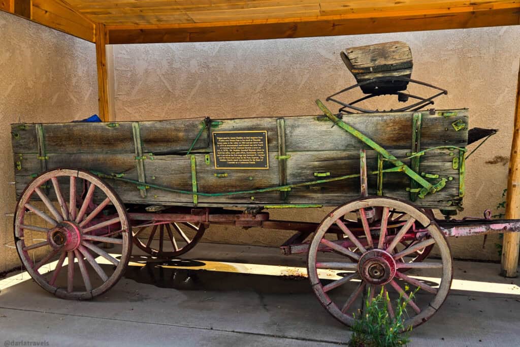 Historic wooden freight wagon with large spoked wheels and brass plaque on display in a covered shelter