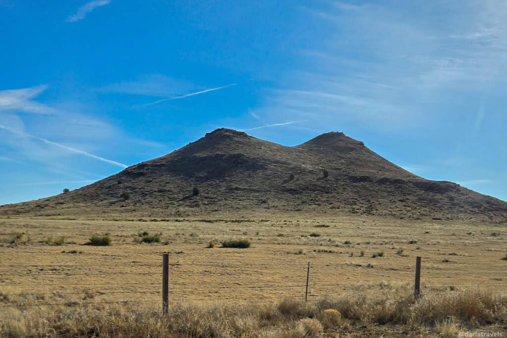 Twin rounded buttes rise from open prairie grassland under a bright blue sky.