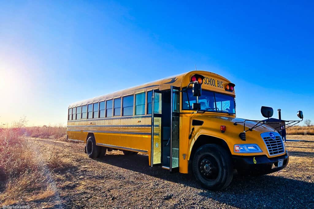 Yellow school bus parked on a gravel road in bright morning light under a clear blue sky