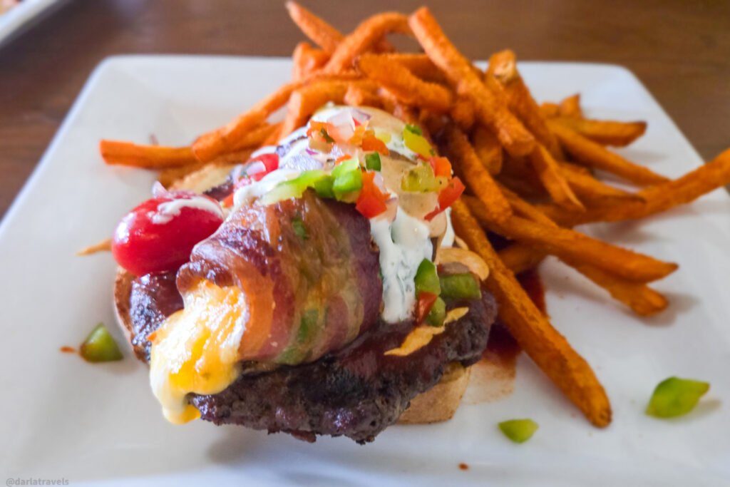 bacon-wrapped anaheim popper and melted cheese, served with a side of sweet potato fries on a square white plate.