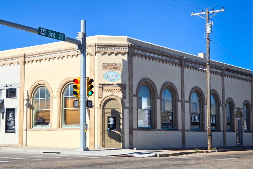 Corner building with arched windows, "Bank of Wray Estd. 1887" signage, and a traffic light on a sunny day.