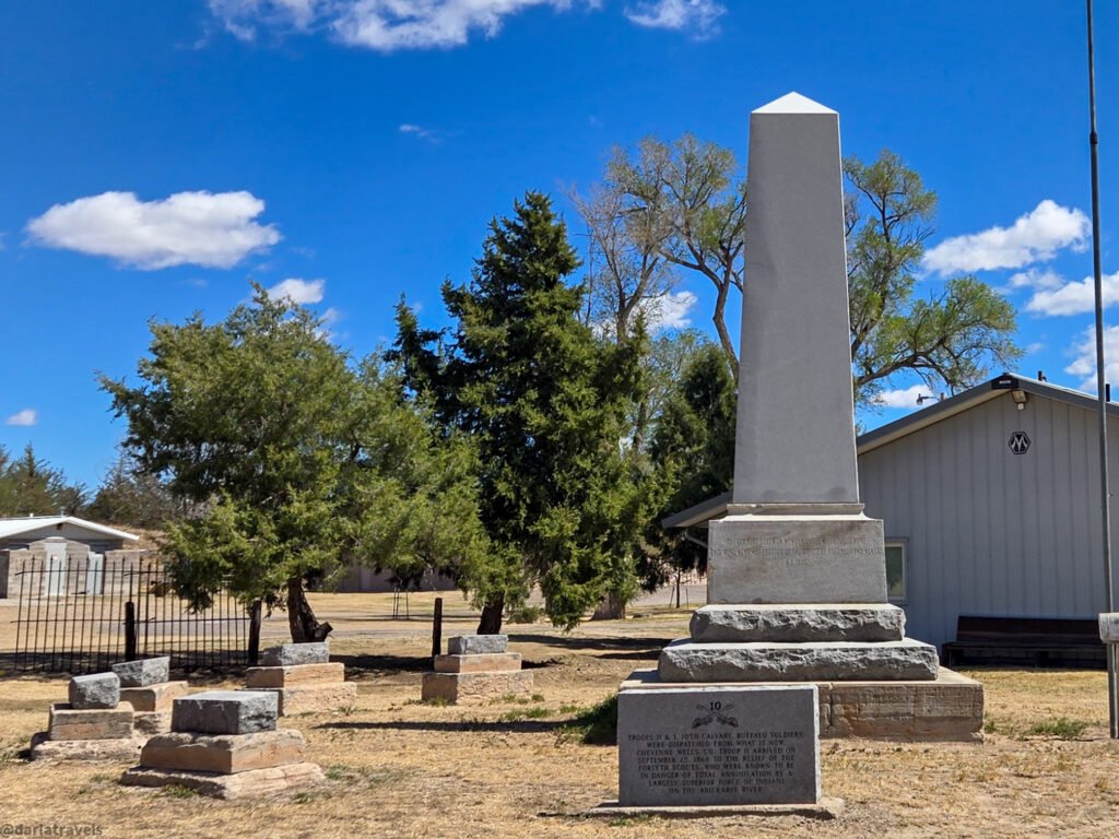 Beecher Island Battlefield Monument with an obelisk, stone markers, trees, and a blue sky