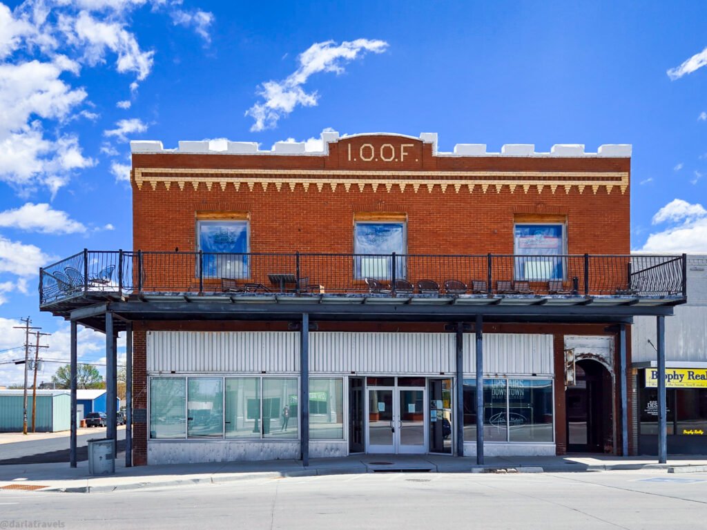 Historic red-brick I.O.O.F. building with a second-floor balcony and ground-floor storefronts