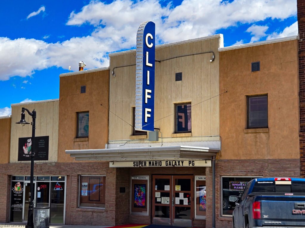 Cliff movie theater with a blue vertical marquee sign under a bright blue sky with clouds.