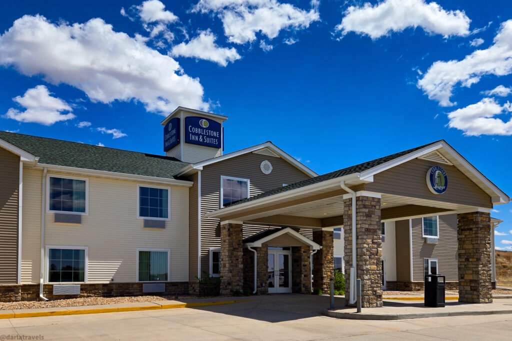 Cobblestone Inn & Suites building with a covered entrance and a blue sky with white clouds.